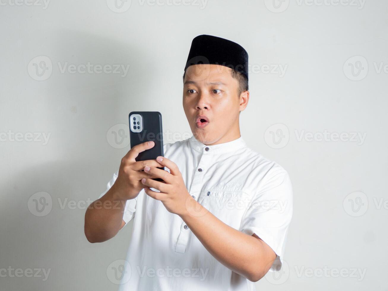 Muslim Asian man shows shocked and surprised expression while holding his phone photo