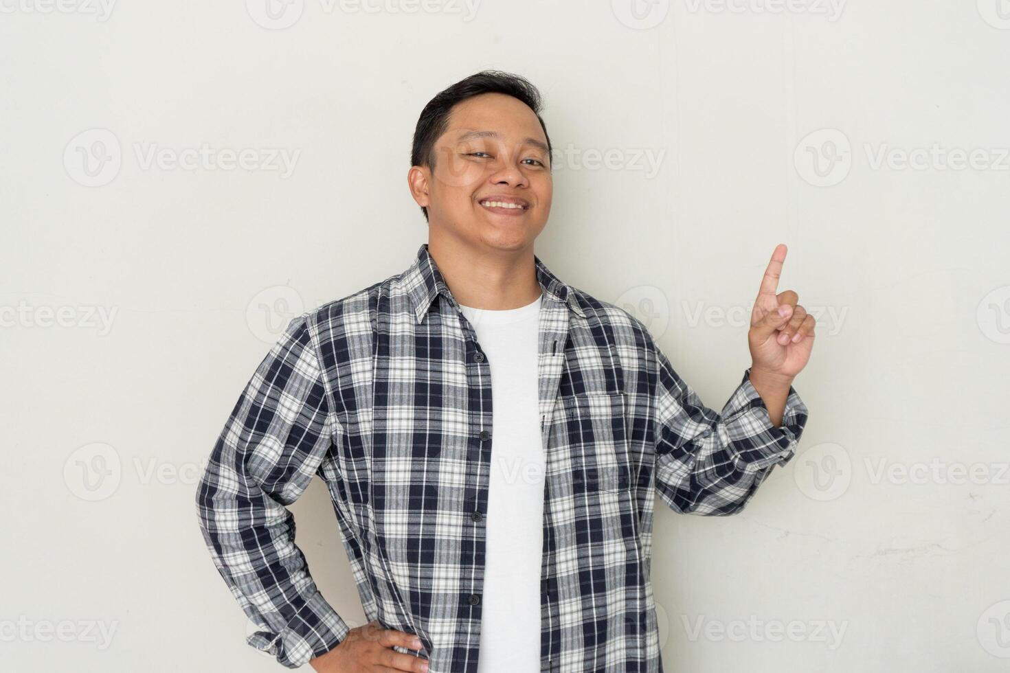 Attractive young Asian man smiling and pointing his finger to the left side. Copy space. photo