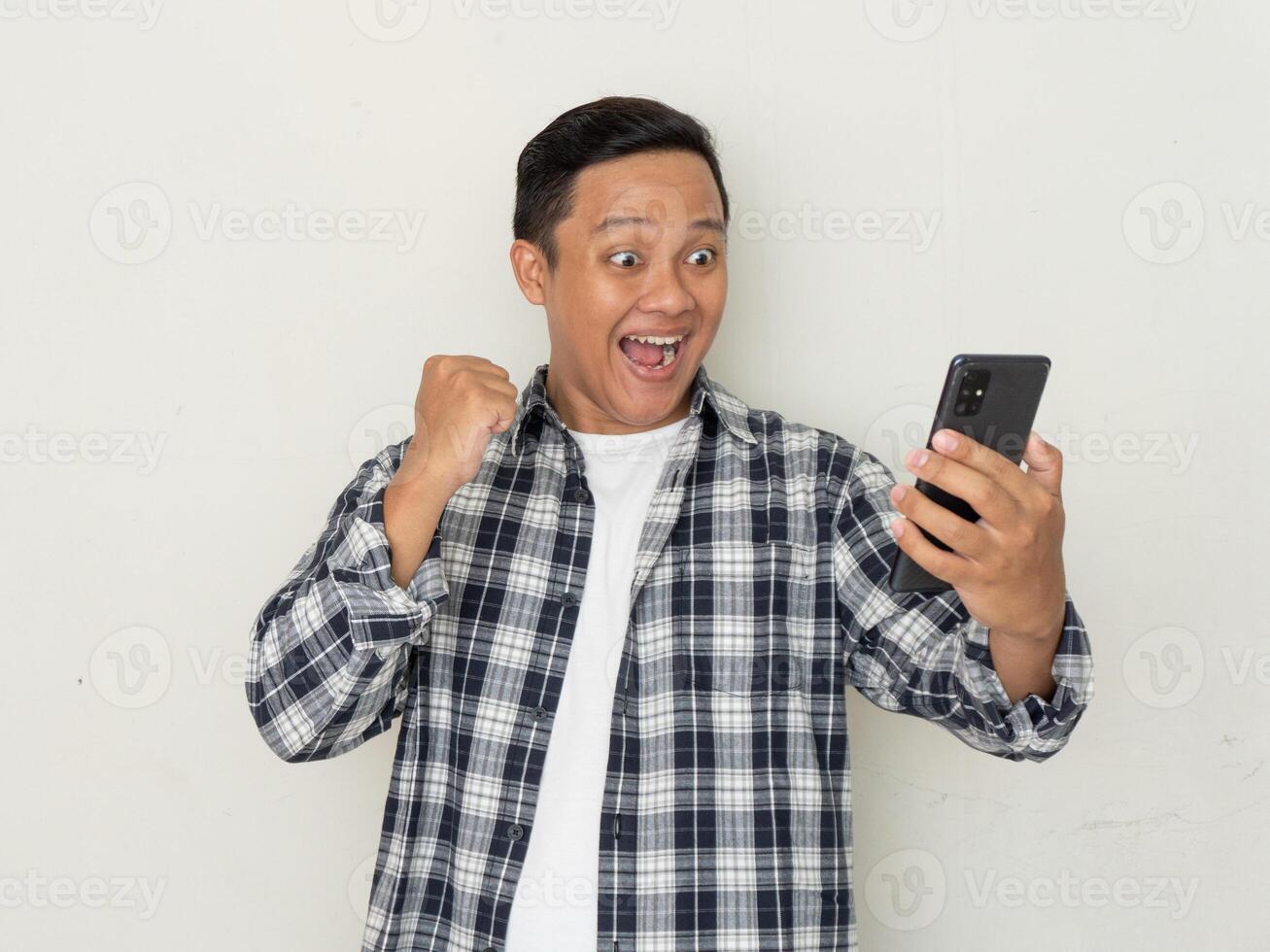 Asian man happy and excited while looking to his phone. Young man surprised and shocked looking to handphone screen photo