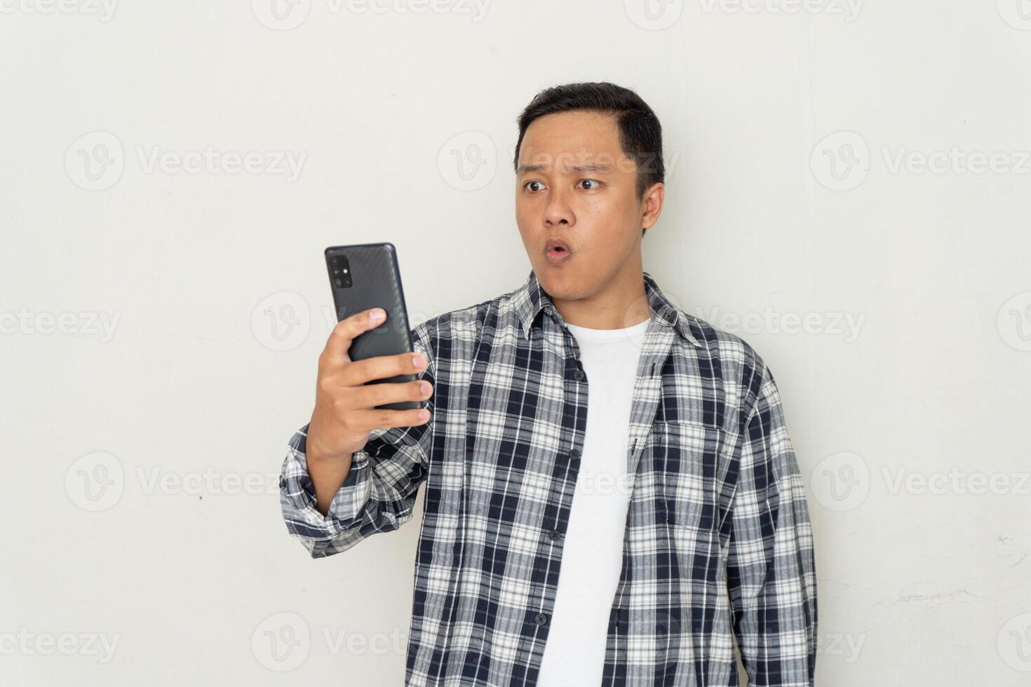 Asian man pointing to mobile phone with afraid and surprised expression. hearing bad news concept photo
