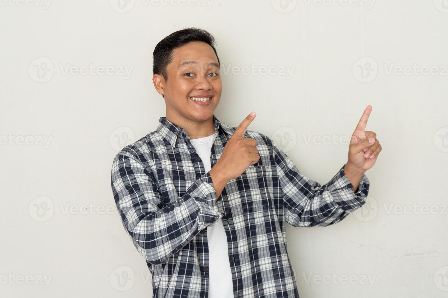 young Asian man smiling and pointing his finger to the side. Copy space. photo