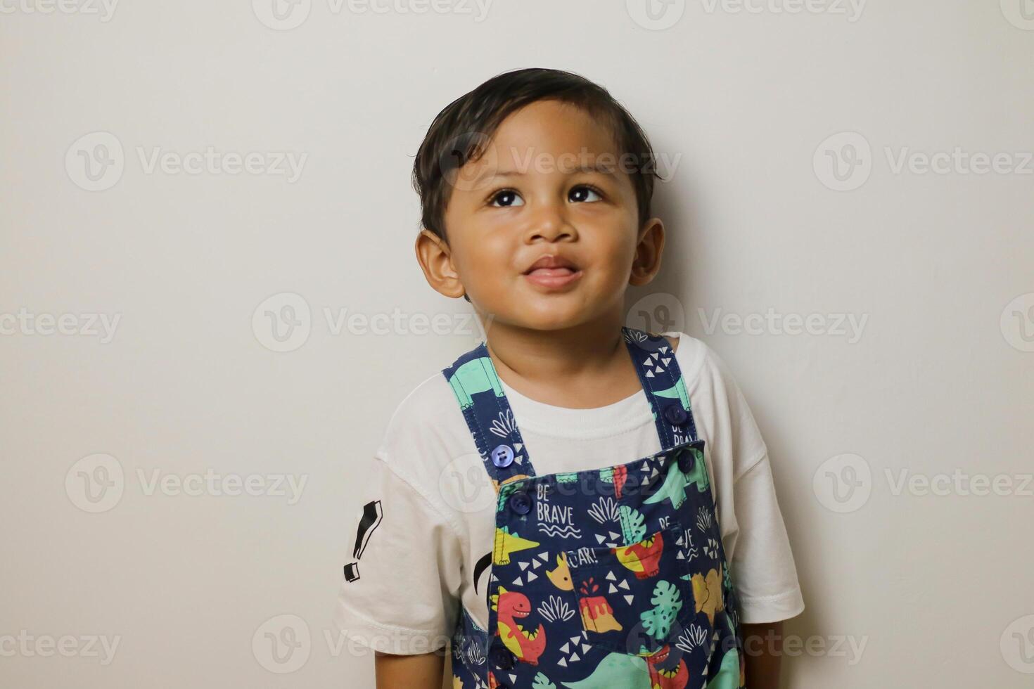 Cute smiling boy in plain white t shirt looking and pointing hand up in isolated studio light white color background photo