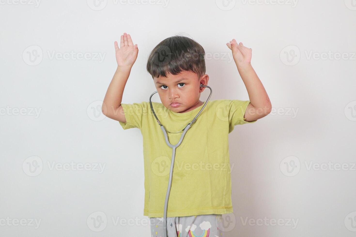 Smiling little boy in medical uniform playing with stethoscope and hands up isolated on white photo