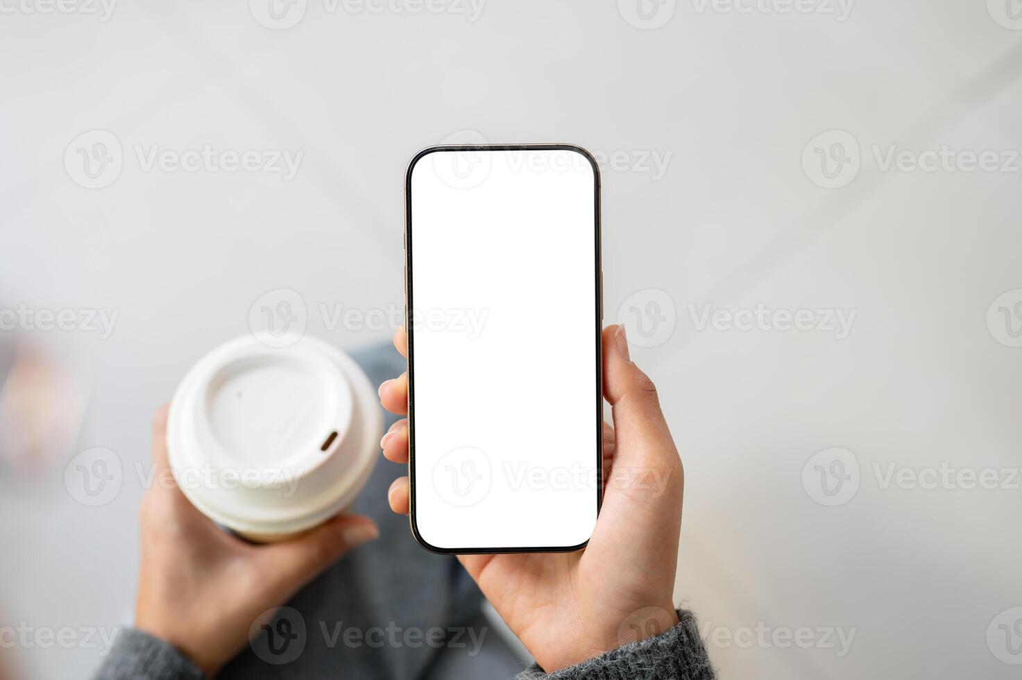 A top view of a woman holding a coffee cup and a smartphone with a white screen mockup. photo