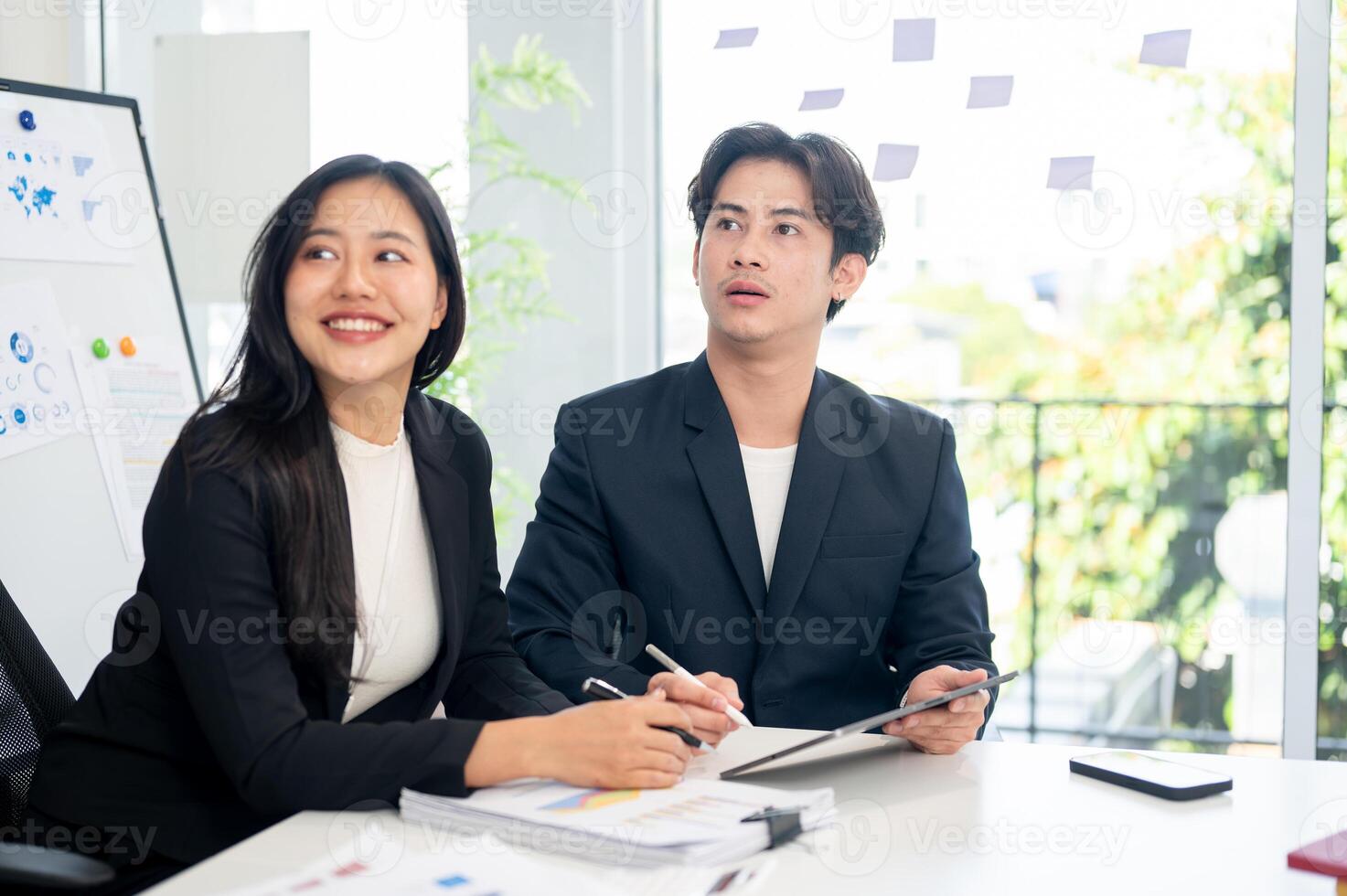 Two positive Asian businesspeople are intently listening to a presentation during a meeting. photo
