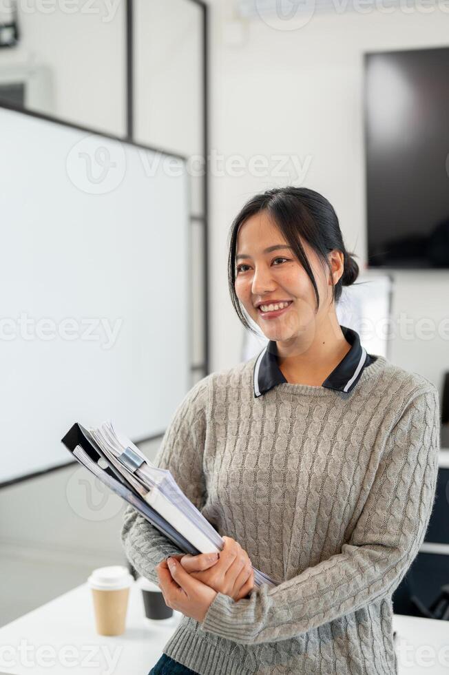 An attractive Asian businesswoman carries documents and files while standing in the office. photo