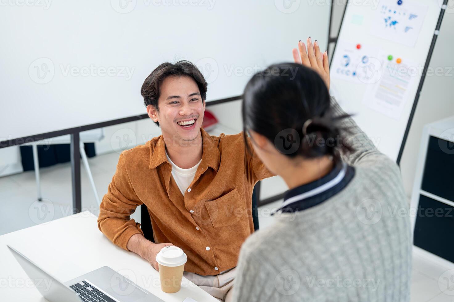 A smiling Asian man gives a high five to his colleague to celebrate their project's success. photo