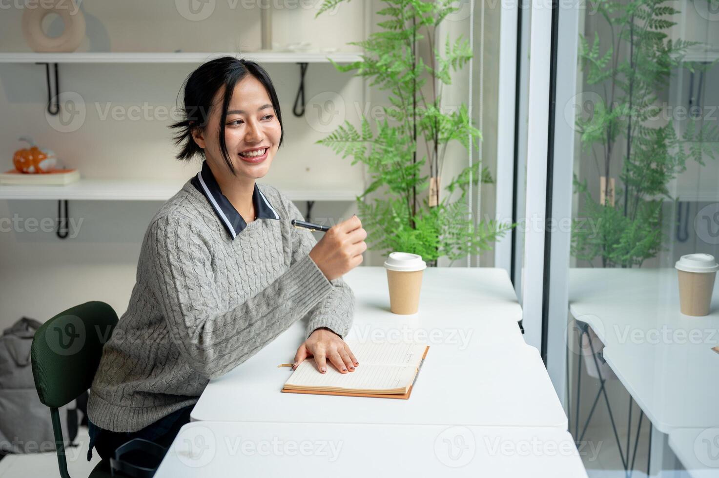 A positive Asian woman sits at a table by the window with her diary placed on the table. photo