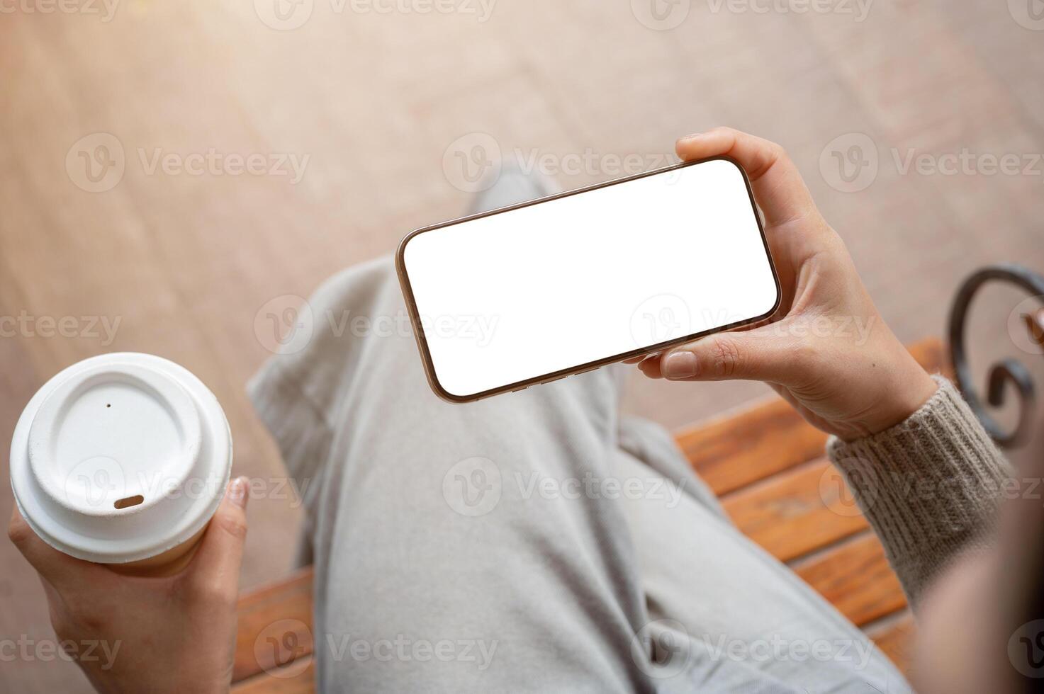 Top view of a woman sits indoors and holds a coffee cup and her smartphone in a horizontal position. photo
