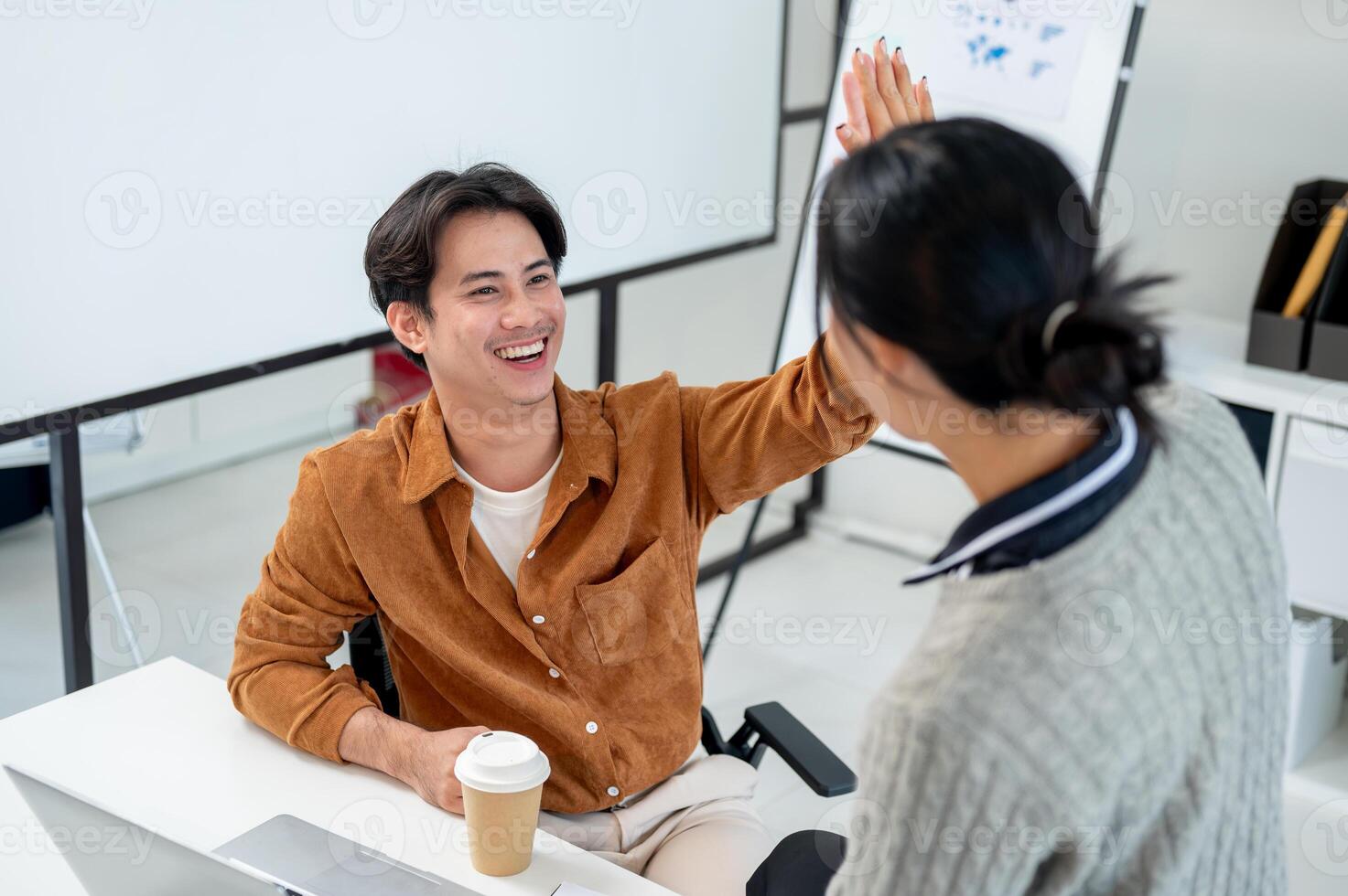 A cheerful Asian man gives a high five to his colleague to celebrate their project's success. photo