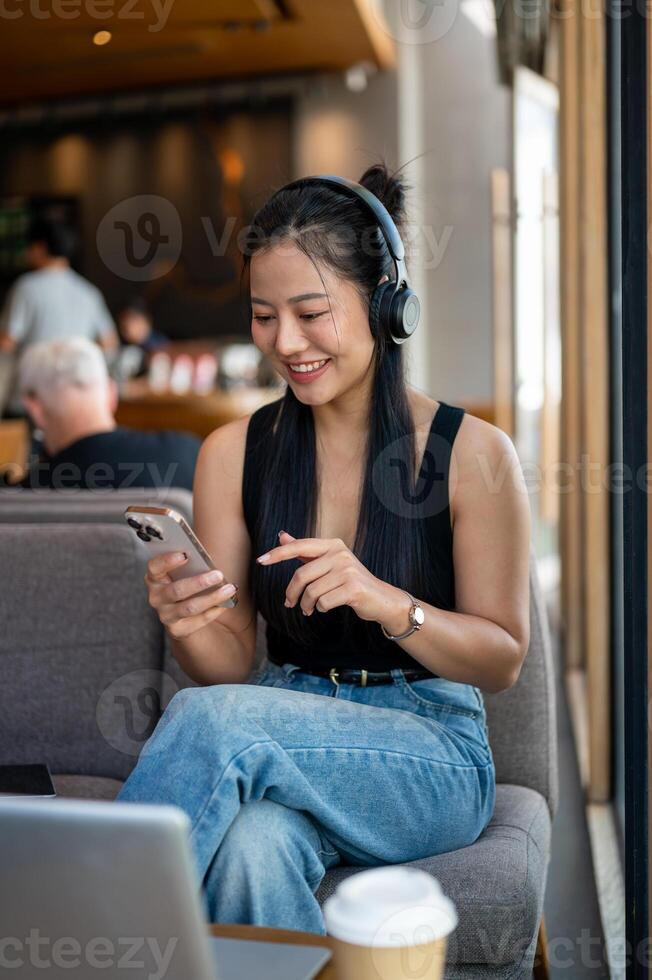 A smiling woman enjoys listening to music while chatting with her friend on her smartphone in a cafe photo
