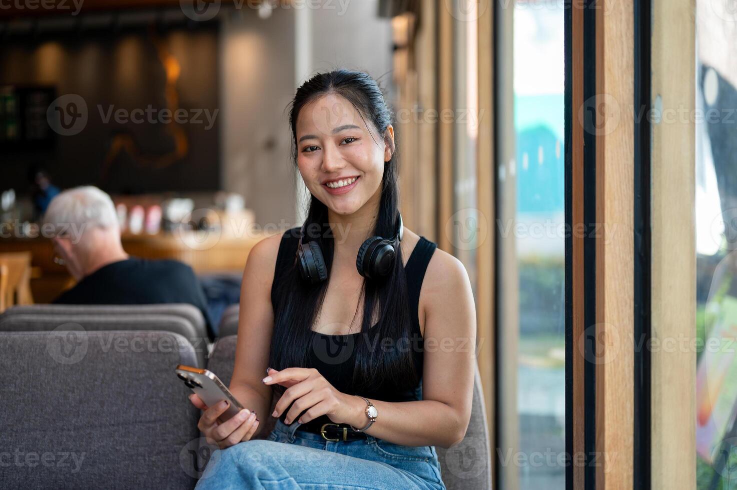 An attractive Asian woman sits on a sofa in a coffee shop, and smiling at the camera. photo
