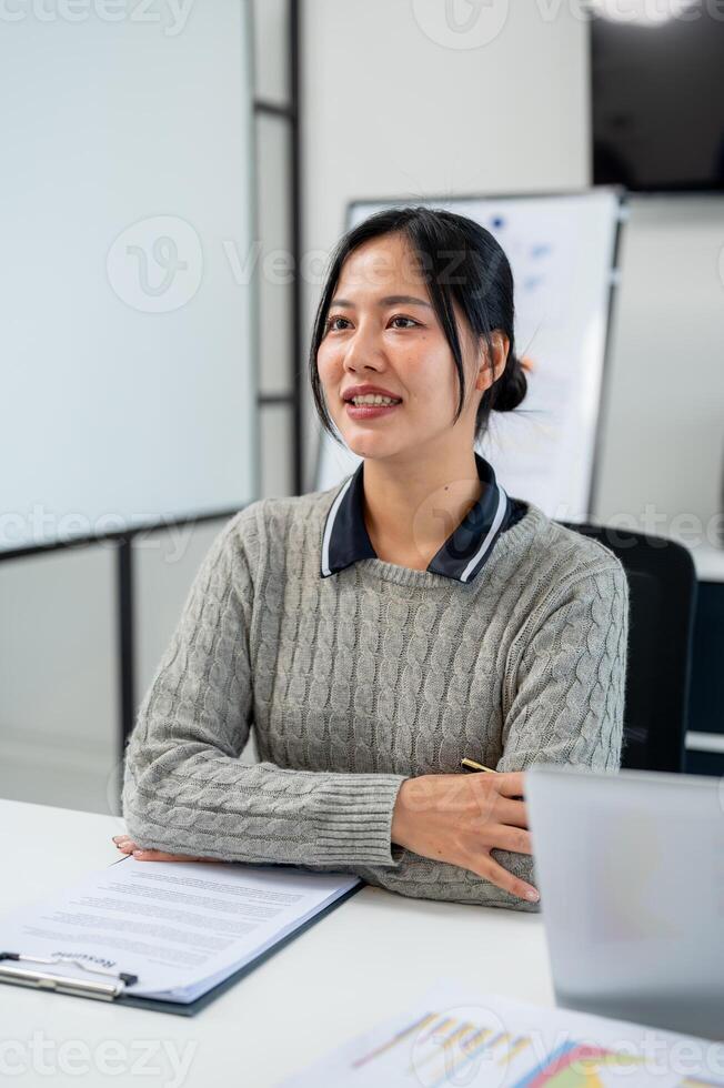 A beautiful Asian businesswoman carefully listens to her colleague's presentation in a meeting. photo