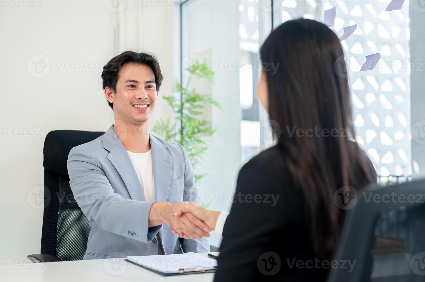 A satisfied Asian businessman shakes hands with a candidate after a job interview in his office. photo