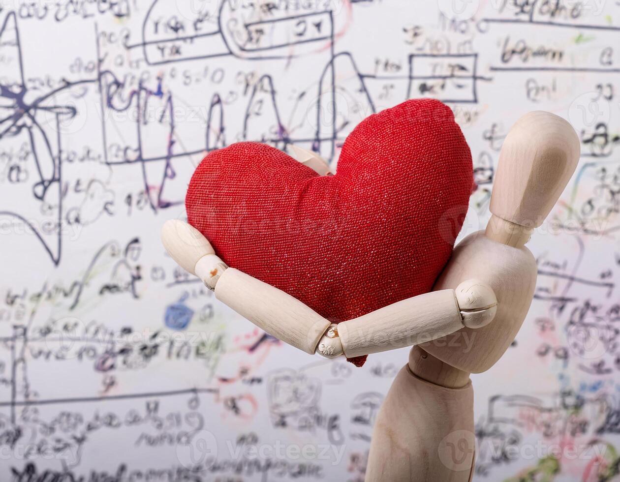 Wooden Mannequin Carrying a Soft Love Symbol with Chalkboard Scribbles in the Background photo
