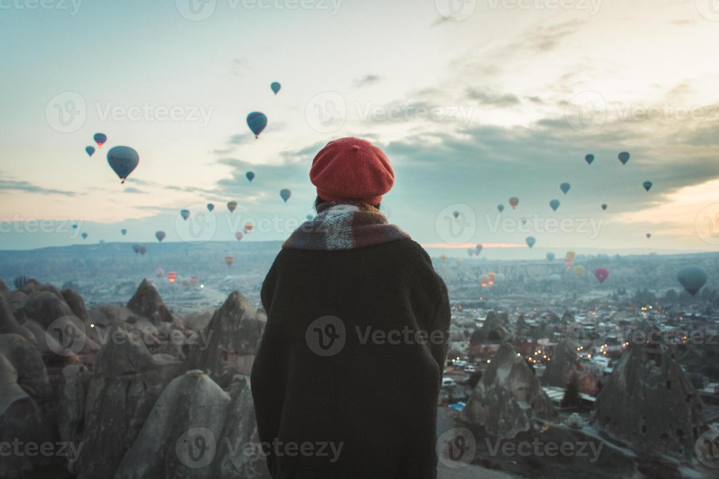 Close up back view Woman looking observe balloon show ,wear fashionable clothing stand on scenic viewpoint watch hot air balloon flight on sunrise with beautiful goreme town and valley background photo