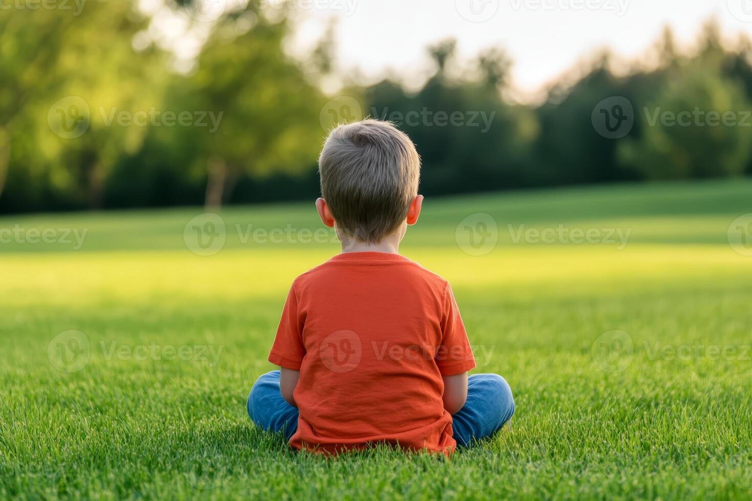 Child sitting peacefully on grass in a sunlit park during a calm evening photo