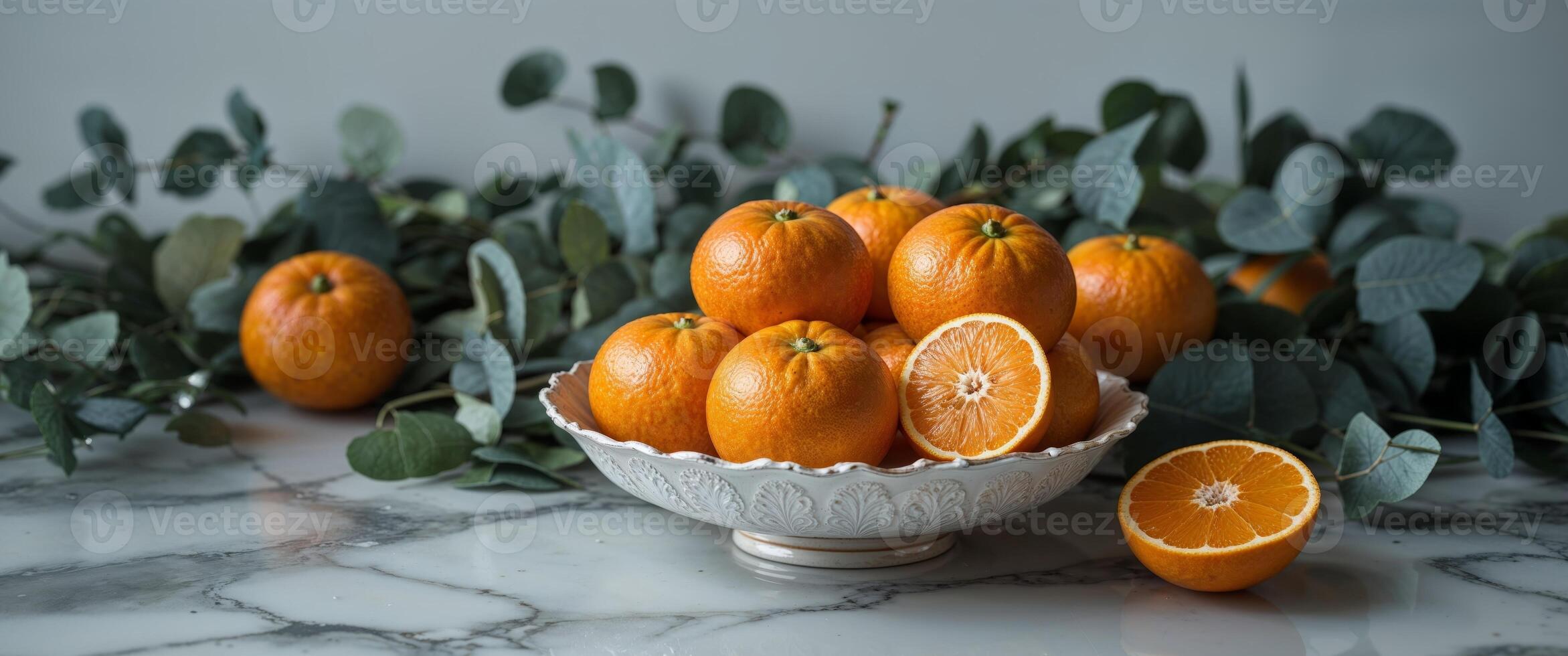 Tangerines in a decorative bowl with a half cut piece on a marble surface surrounded by greenery for a fresh and vibrant look. photo