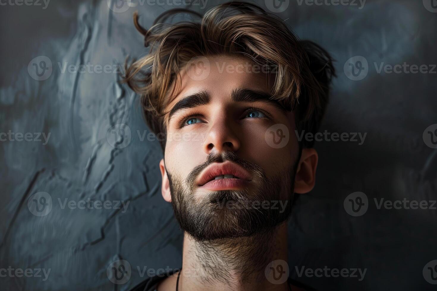 Handsome young man with blue eyes and brown hair lying down, looking up, on a textured gray background photo