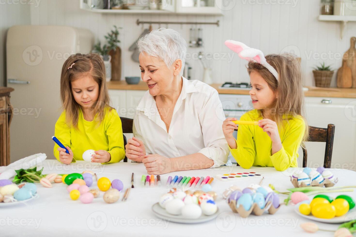 Happy Easter. Two little girls sisters twins grandmother painting eggs enjoying time together. Happy family grandma granddaughters child kids preparing for Easter. Spring Christian festival tradition photo