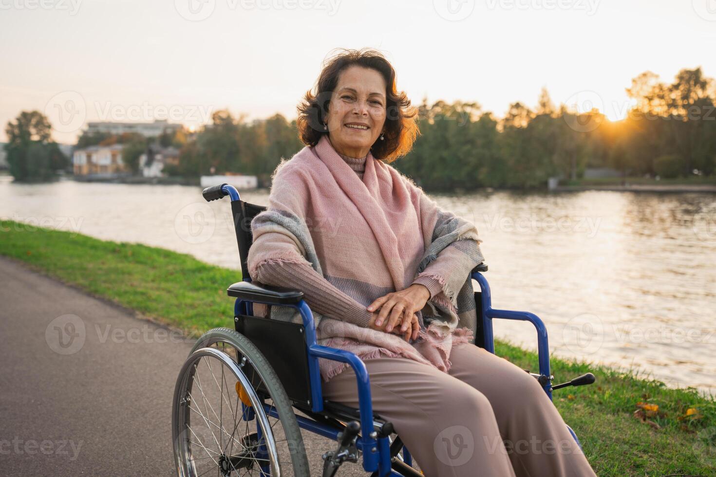 Happy senior woman in wheelchair smiling enjoying freedom walking on road in city park outdoor. Old cheerful positive woman in chair for people with disability. Disability disease rehabilitation photo