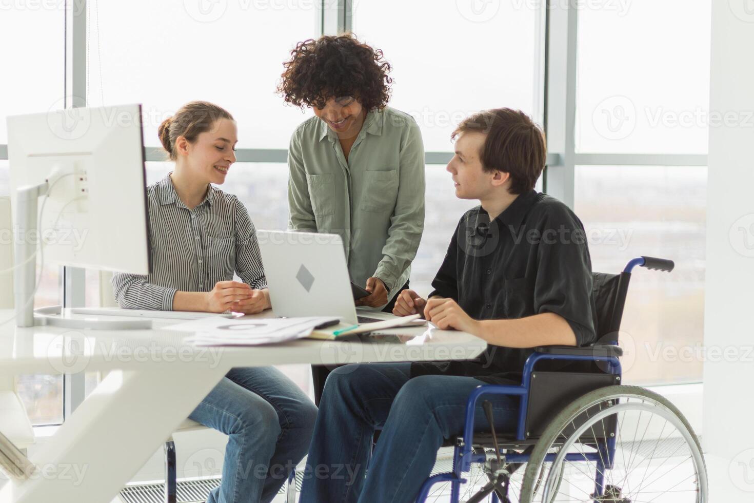 Teamwork brainstorm. Diverse multiracial colleagues man in chair for people with disability working together. Group of people sitting in creative office discussing business. Young professional team photo