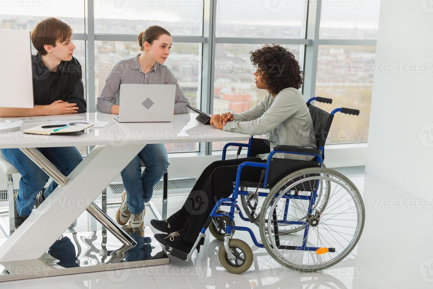 Teamwork brainstorm. Diverse multiracial colleagues woman in chair for people with disability working together. Group of people sitting in creative office discussing business. Young professional team photo