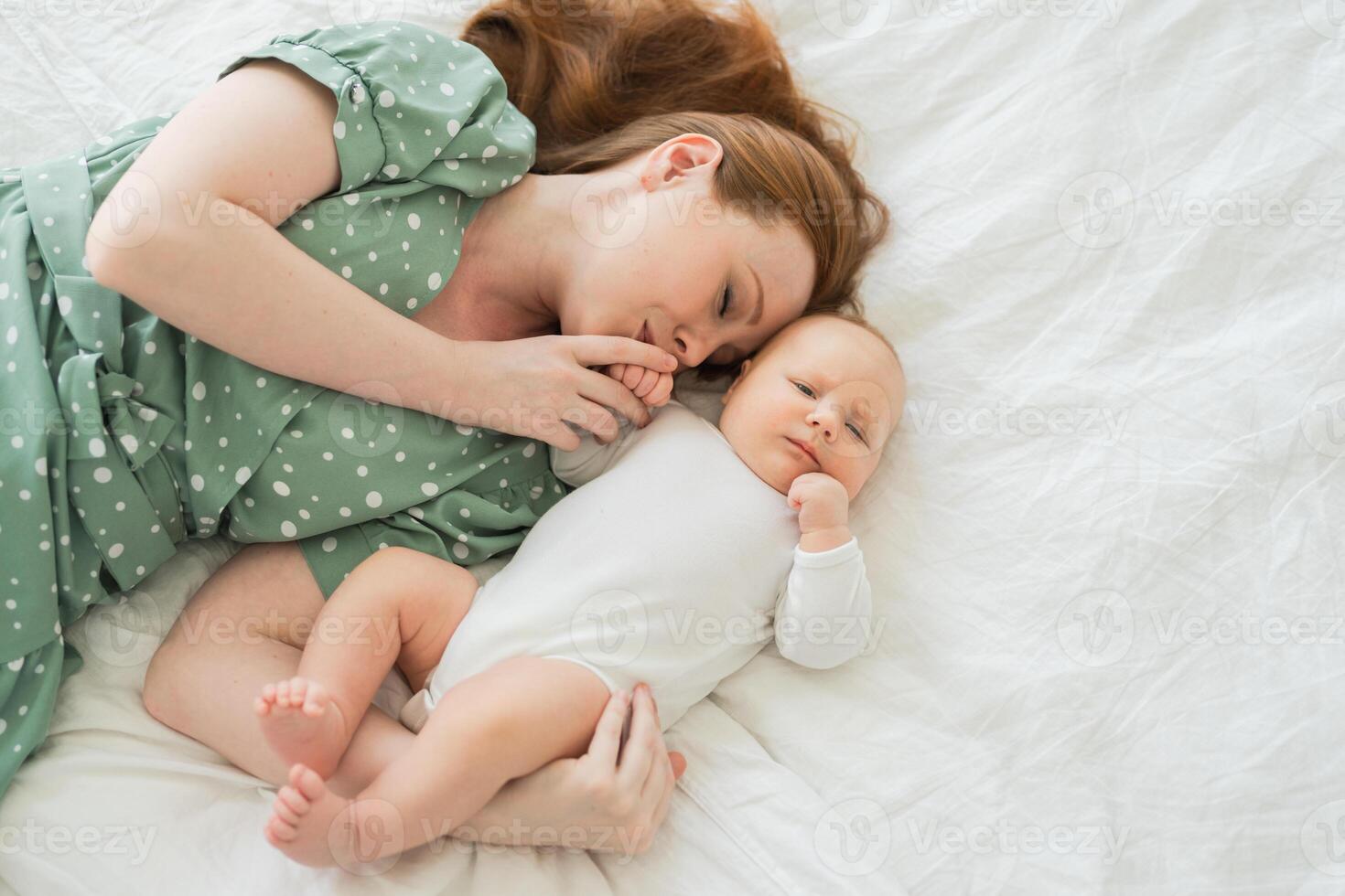 Happy family at home. Mother playing with little toddler child on bed. Mom baby relax playing having fun together. Mother hugs baby with love care. Mom of breast feeding baby rest in living room photo