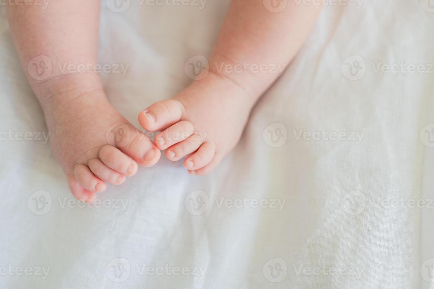 Tiny newborn infant baby feet and toes on white background. Soft newborn baby foot legs under the white blanket. Close up of infant barefeet. Maternity tenderness parenthood birthday. Happy Family photo