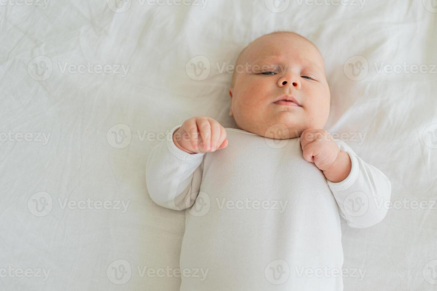 Happy baby. Cute little newborn girl with smiling face lying on bed in bedroom. Infant baby resting playing lying down on white blanket at home. Motherhood happy child childcare concept photo