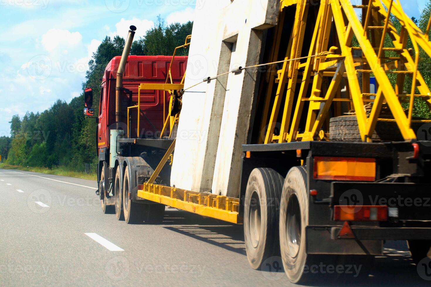 A panel truck with a semi-trailer transports reinforced concrete slabs for building a house. Cargo transportation in summer along the road against the backdrop of the forest. Copy space for text photo