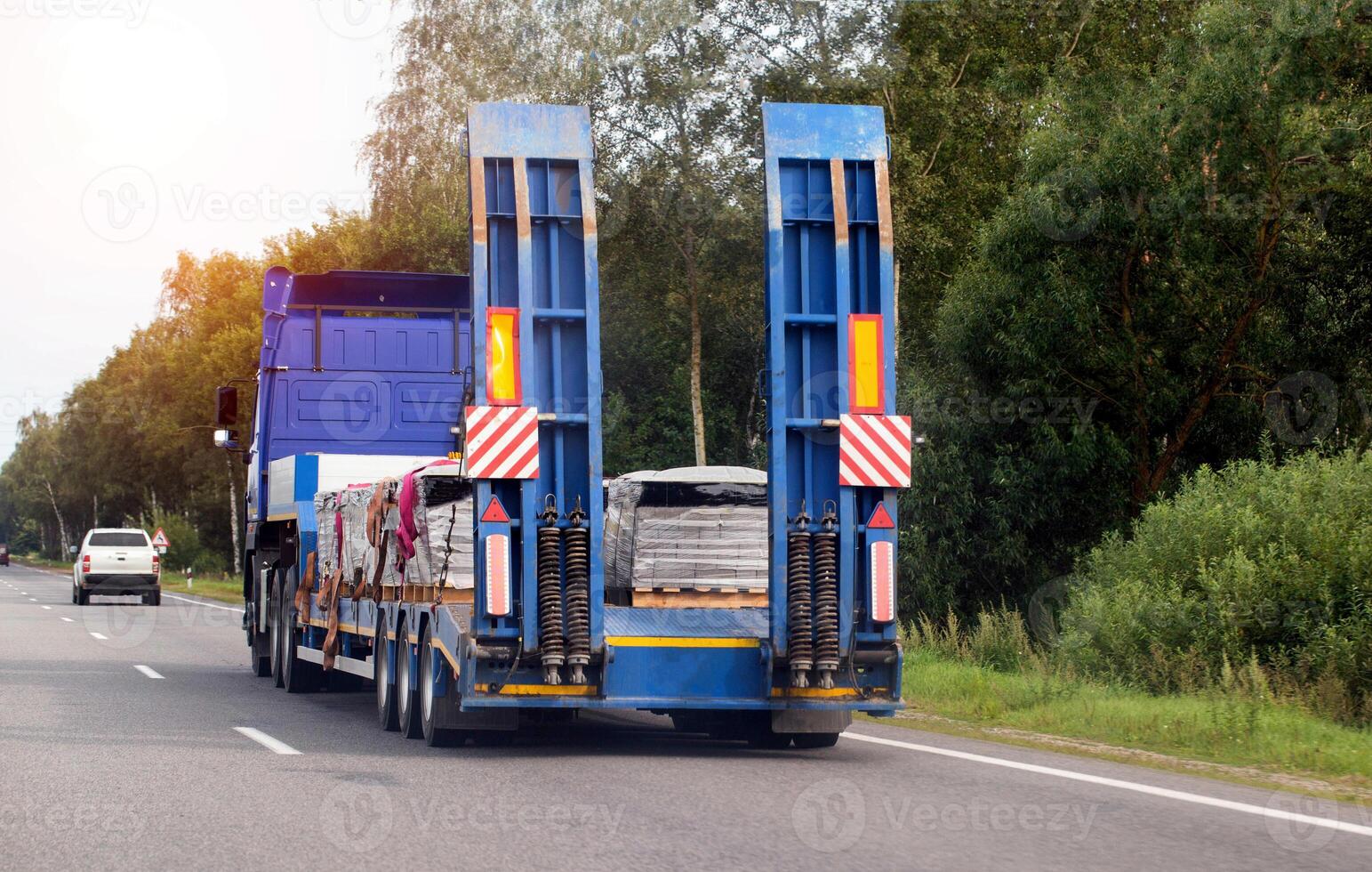 A modern truck with a low-loader transports paving slabs along a highway in the summer. Trawl trailer services and rental photo