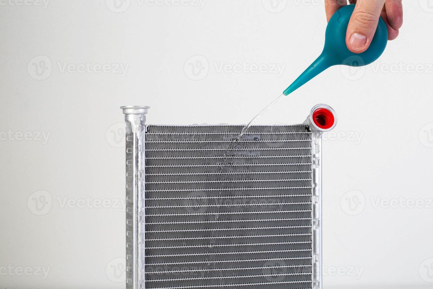 A jet of water from a syringe pours onto a car radiator. The concept of cleaning and flushing car radiators from pollution. Clogged radiator cells. Copy space for text photo