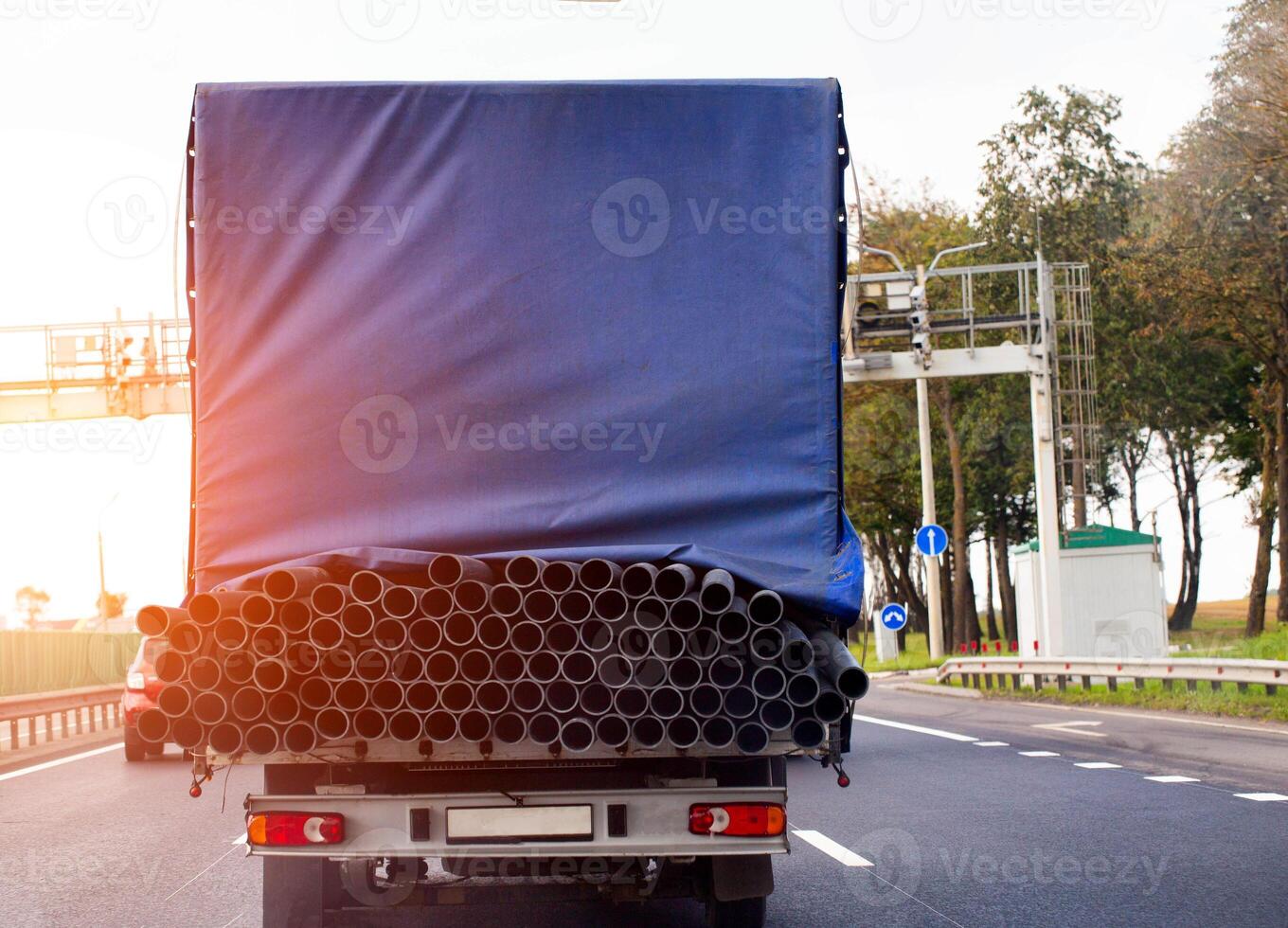 A tilt van transports an oversized cargo of metal pipes along the road against the backdrop of a sunset, close-up photo