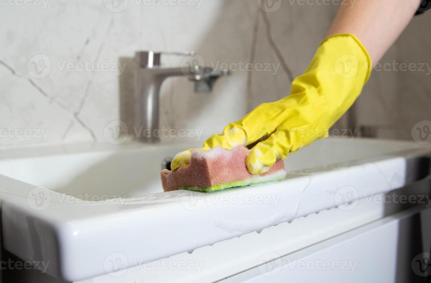 A girl's hands in yellow gloves wash the bathroom sink with a cleaning product for a pleasant smell and shine, close-up. photo