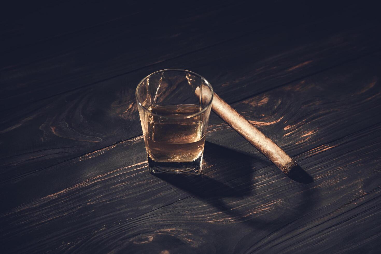 A glass of whiskey and a cigar on a wooden table photo