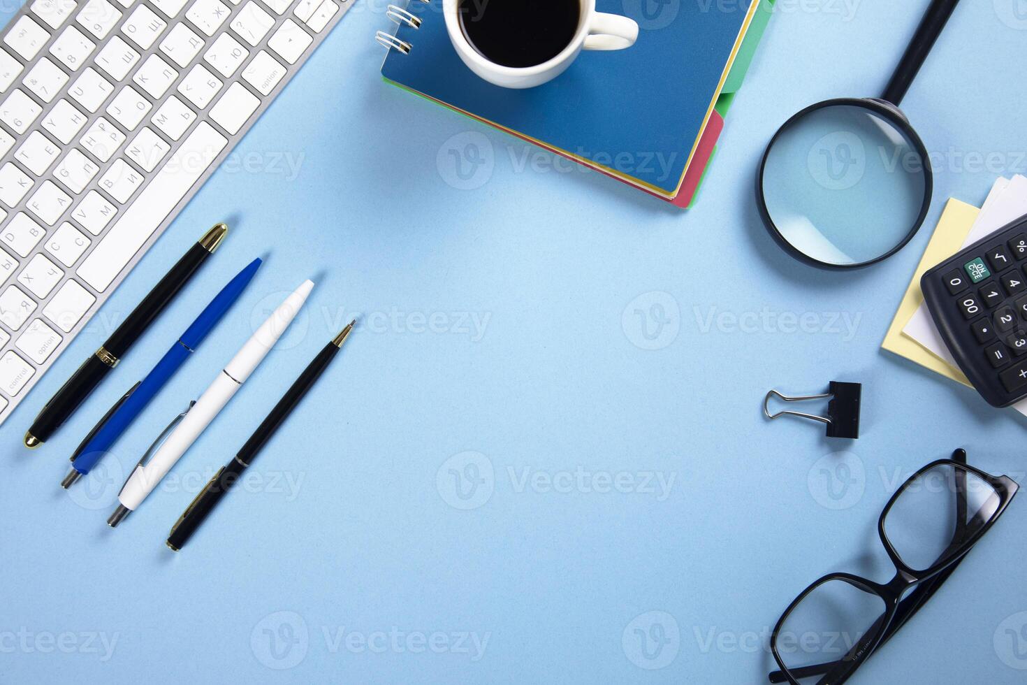 A desk with a keyboard, mouse, pen, glasses, and a notebook photo