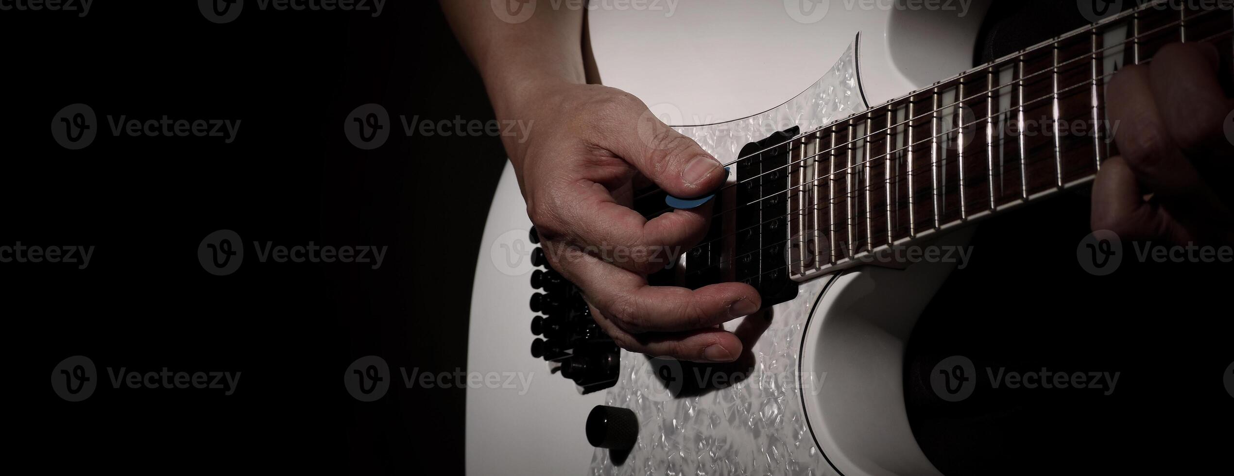 Guitarist Playing Guitar In Studio Low key of man hand play white electric guitar for songs and cover music or skill practice. Close up of musician playing guitars instrument against black background photo