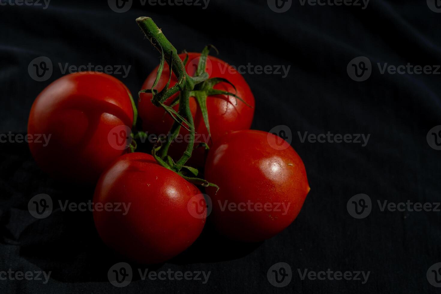 Four red ripe tomatoes on one green branch on a black table photo