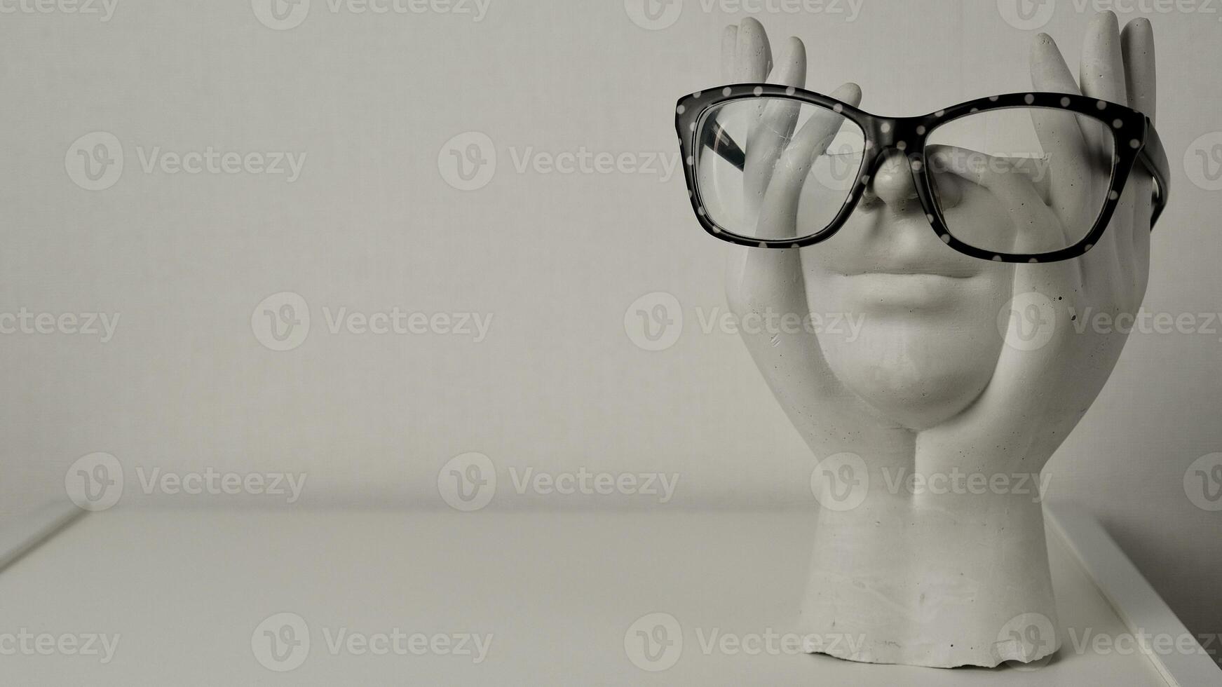 Close-up of a white headless statuette wearing glasses with white dots on a light solid background photo