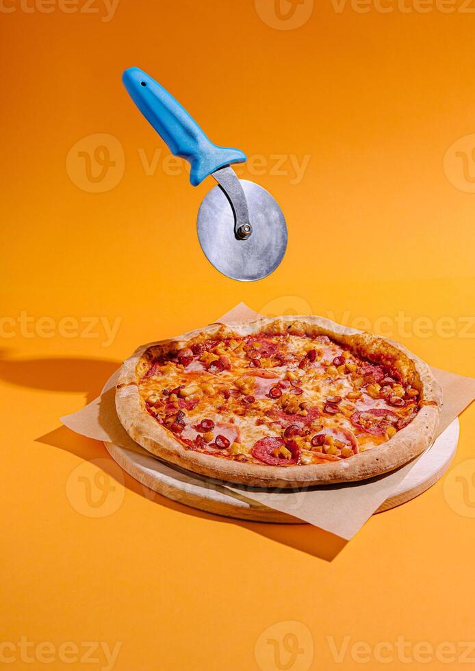 Pizza with vibrant orange background and a pizza cutter floating above ready for slicing photo