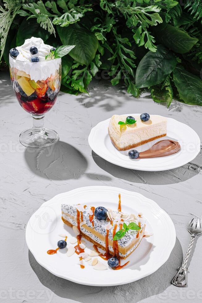 Desserts beautifully arranged on white plates with fresh fruits and toppings in a green setting photo