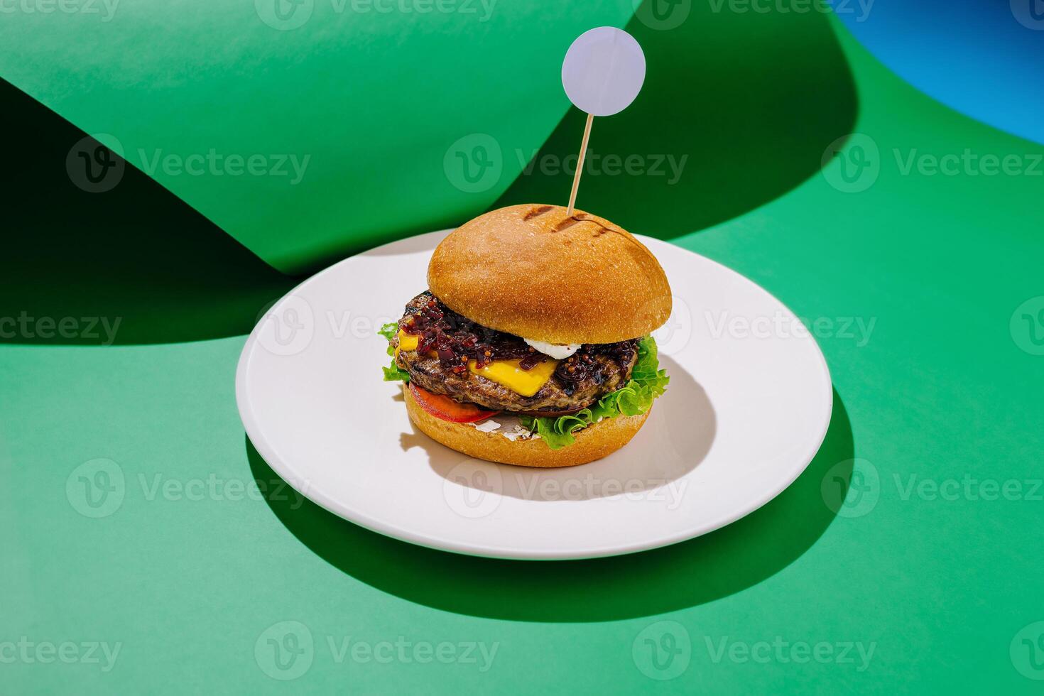 Gourmet hamburger with crispy lettuce, cheese, and tomato served on a white plate against a green backdrop photo
