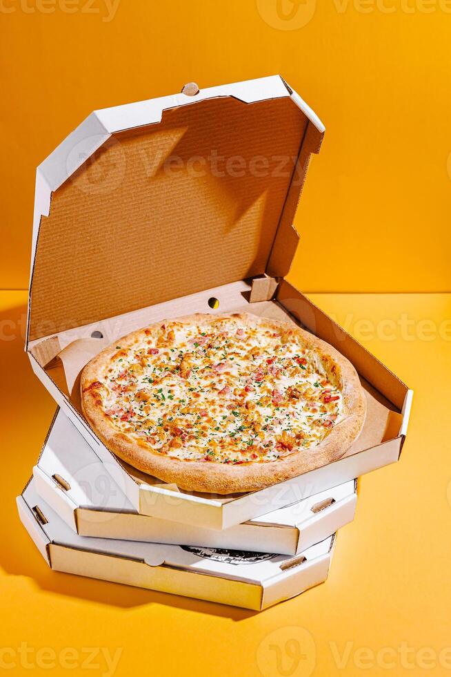 Delicious freshly baked pizza in an open delivery box against a bright yellow background photo