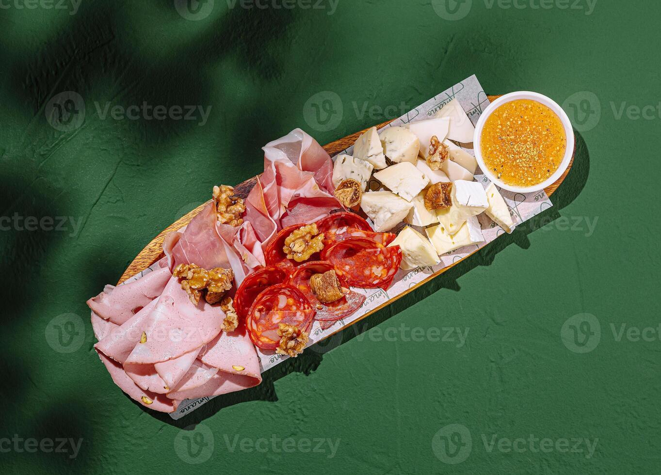 Charcuterie board featuring assorted meats, cheeses, and a sweet dip on a green tabletop during a casual gathering photo