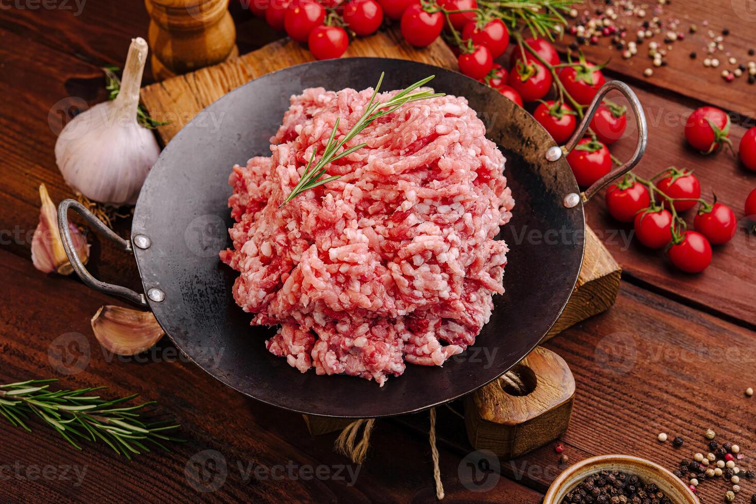 Freshly minced meat on a wooden table surrounded by spices and tomatoes ready for cooking photo