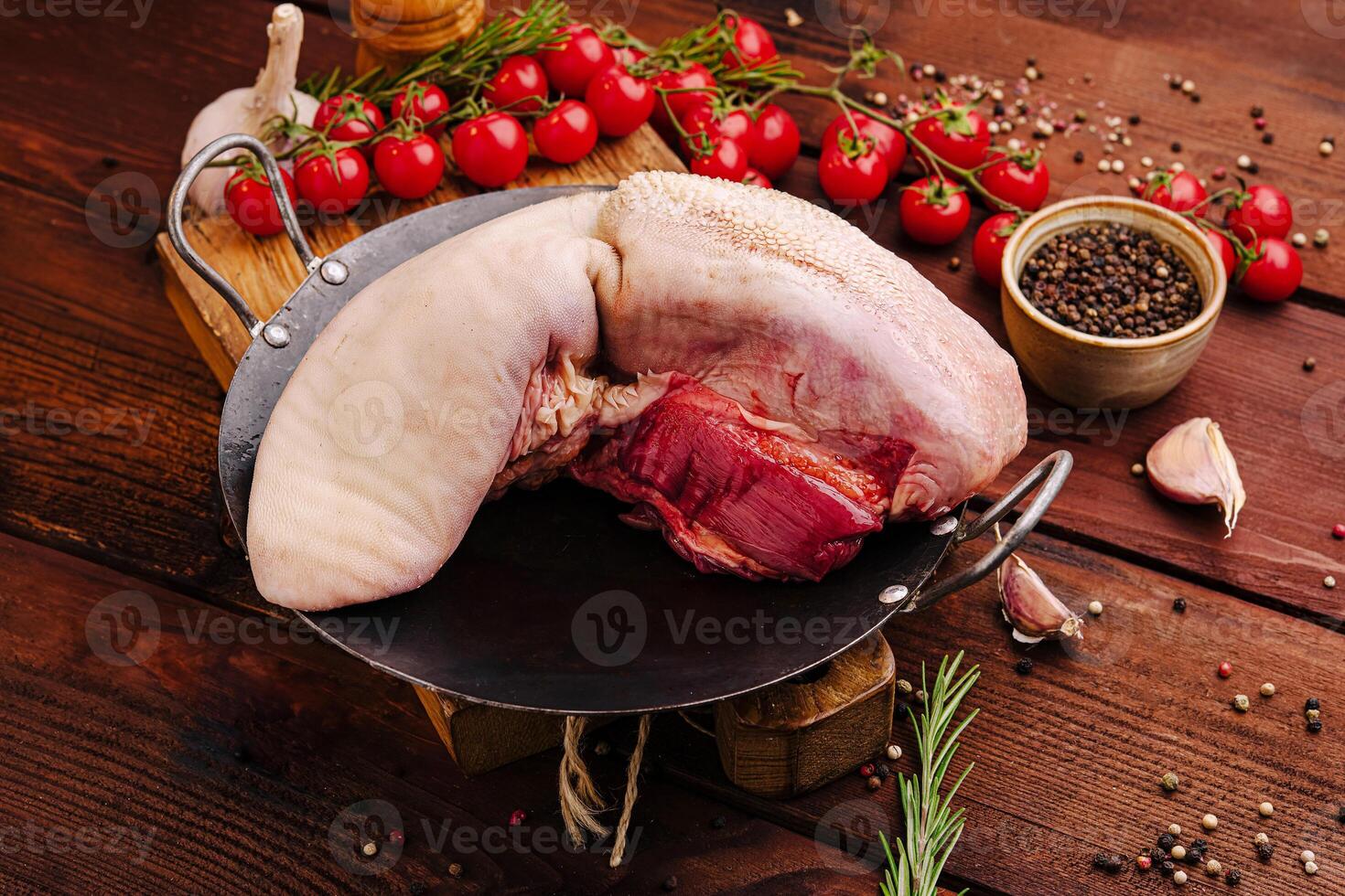 Fresh meat cut displayed on a wooden table with tomatoes, herbs, and spices in a rustic kitchen setting photo