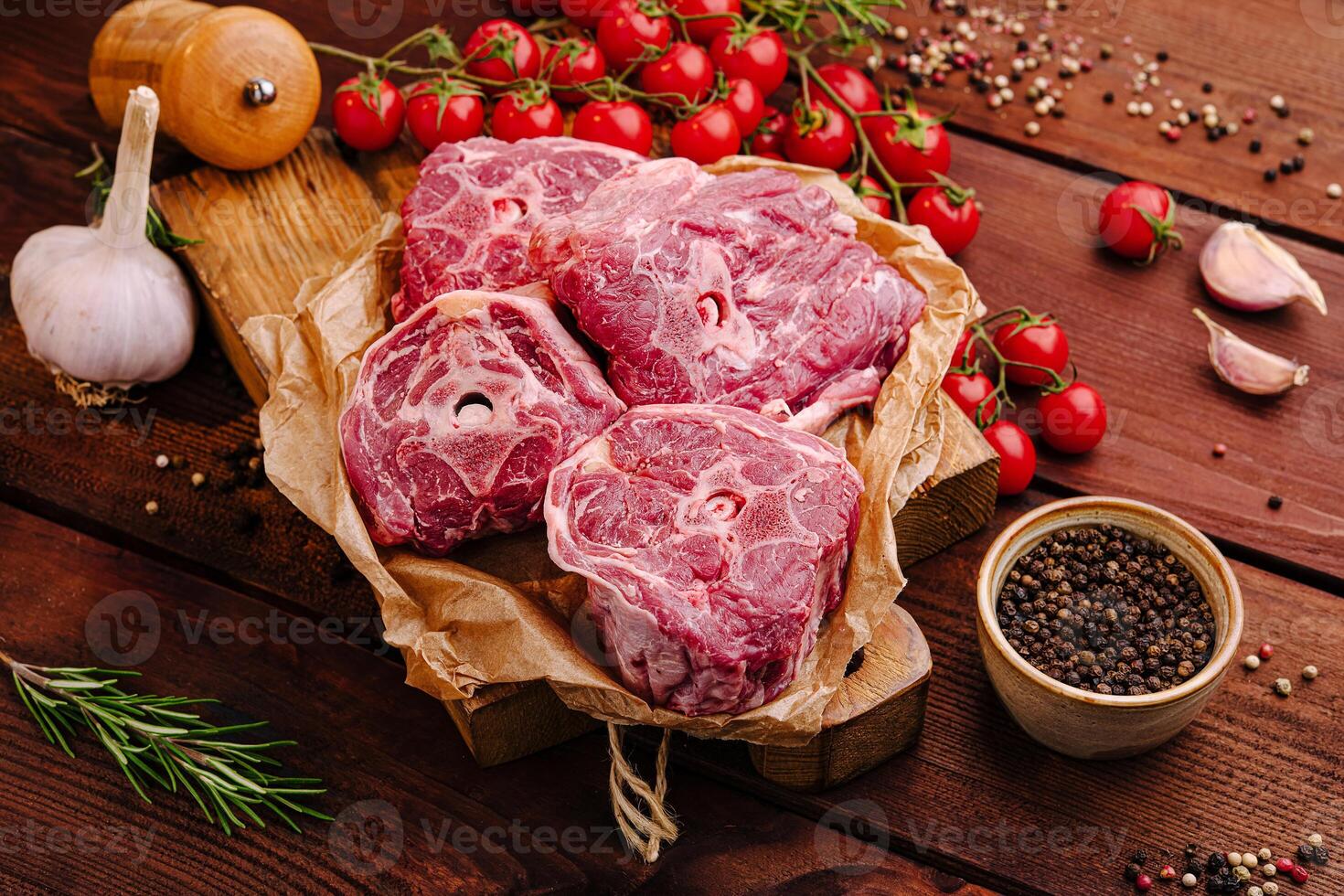 Fresh cuts of meat arranged on a wooden board with herbs, spices, and cherry tomatoes ready for cooking photo