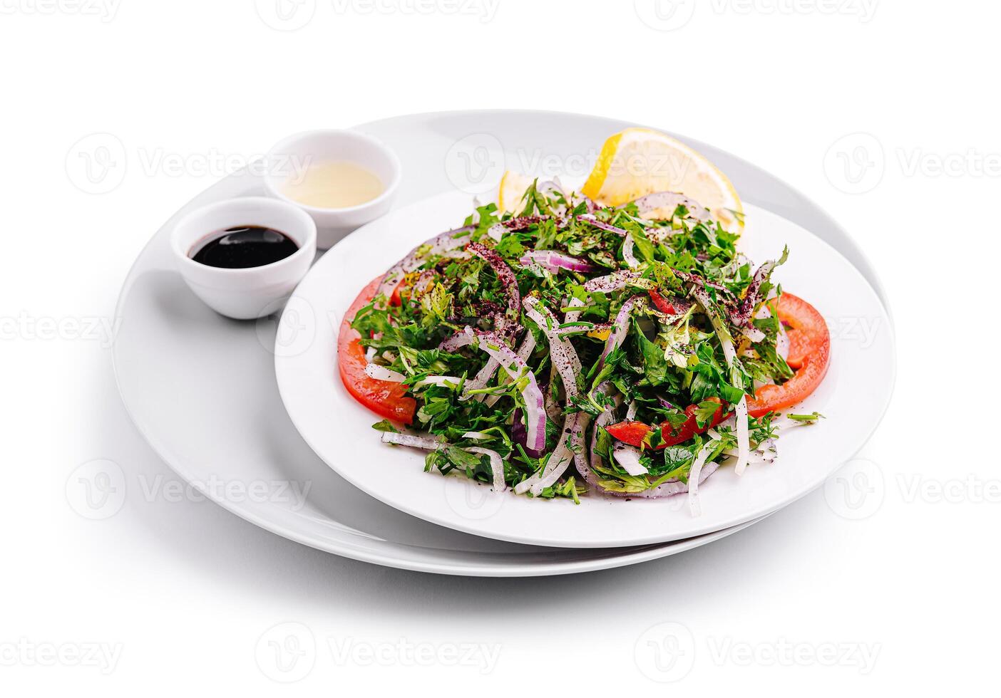 Fresh mixed salad served on a white plate with dressing choices and lemon wedge photo
