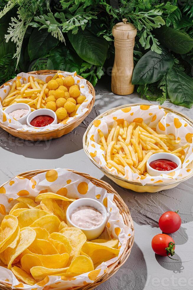 Assorted snacks served in baskets with dips on a table surrounded by greenery photo
